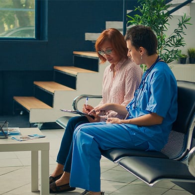 Two nurses, one in scrubs, discuss a patient's chart earnestly, embodying the principle of veracity in nursing through honest communication in a clinic waiting area. Two nurses, one in scrubs, discuss a patient's chart earnestly, embodying the principle of veracity in nursing through honest communication in a clinic waiting area.