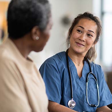 A cheerful nurse in blue scrubs takes notes on a clipboard while engaging with an elderly patient in a clinic room, signifying a caring and professional nurse-patient interaction. A cheerful nurse in blue scrubs takes notes on a clipboard while engaging with an elderly patient in a clinic room, signifying a caring and professional nurse-patient interaction.