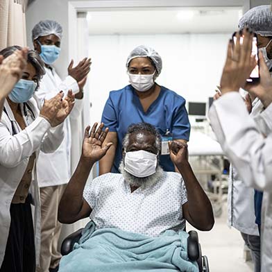 Elderly male patient is being wheeled out of the hospital and hospital staff have lined the hallway and are clapping in happiness for his recovery. Elderly male patient is being wheeled out of the hospital and hospital staff have lined the hallway and are clapping in happiness for his recovery.